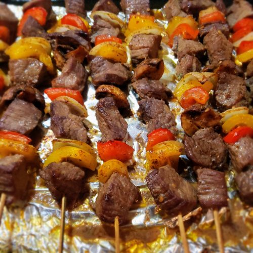 Close-up-of-juicy-grilled-beef-skewers-with-colorful-bell-peppers,-onions-and-mushrooms-resting-on-a-platter