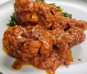 A-close-up-shot-of-juicy-red-tomato-chicken drumsticks-coated-in-a-savory-sauce-garnished-with-fresh-cilantro.