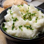 A-close-up-of-a-bowl-of-fluffy,-ultra-smooth-mashed-potatoes-topped-with-a-pat-of-melting-butter-and-fresh-chives.
