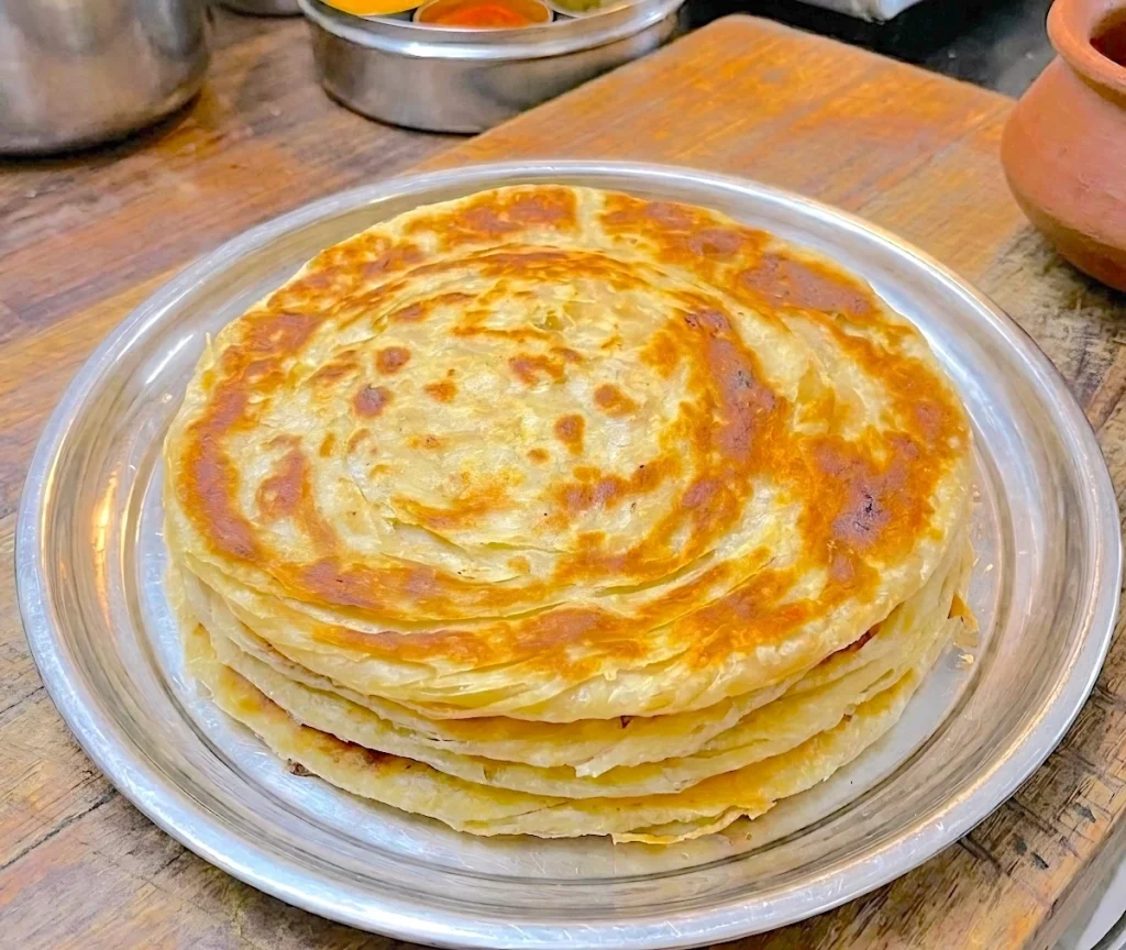 A-tall-stack-of-warm,-golden-brown-soft-layered-chapatis-with-visible,-flaky,-pull-apart-layers-showing-on-the-sides,-served-on-a-rustic-plate.