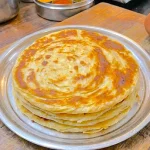 A-tall-stack-of-warm,-golden-brown-soft-layered-chapatis-with-visible,-flaky,-pull-apart-layers-showing-on-the-sides,-served-on-a-rustic-plate.